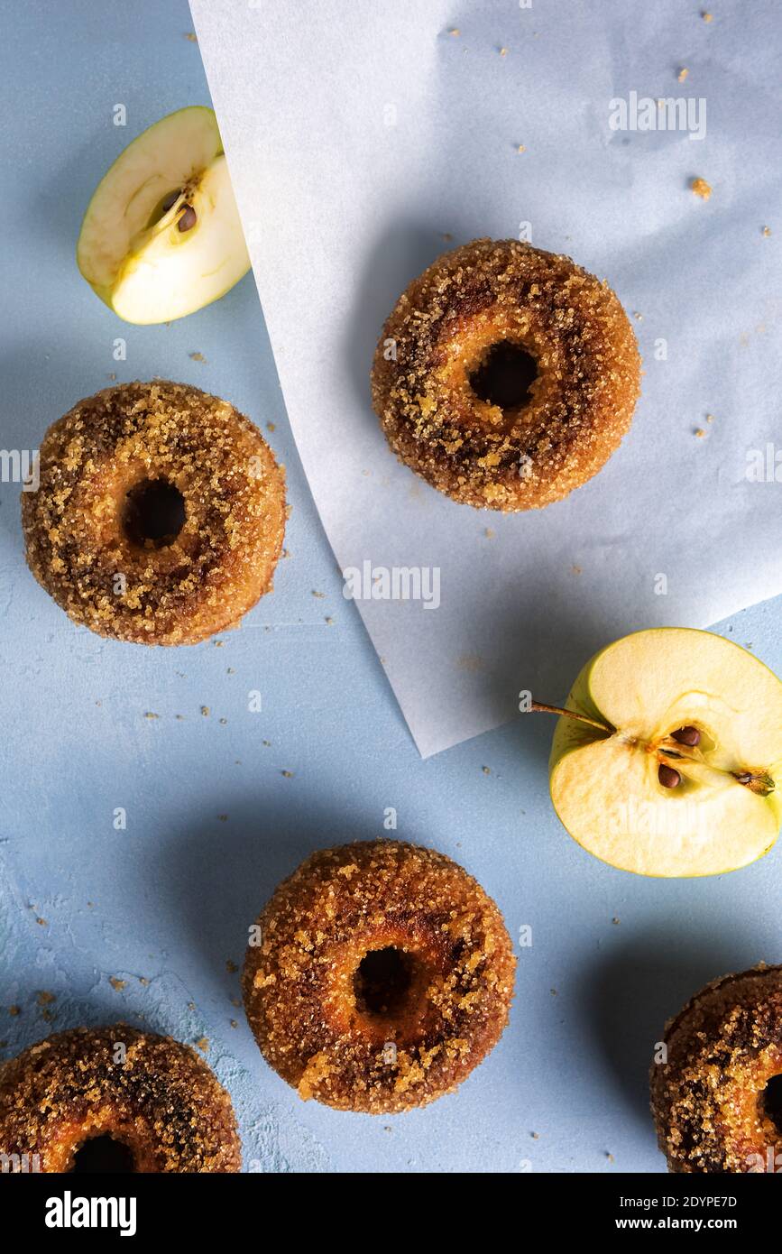 Close-up of homemade sugared apple cider donuts and cut apple on baking paper sheet and blue table. Ready to eat snack. Small batch artisanal food. Di Stock Photo