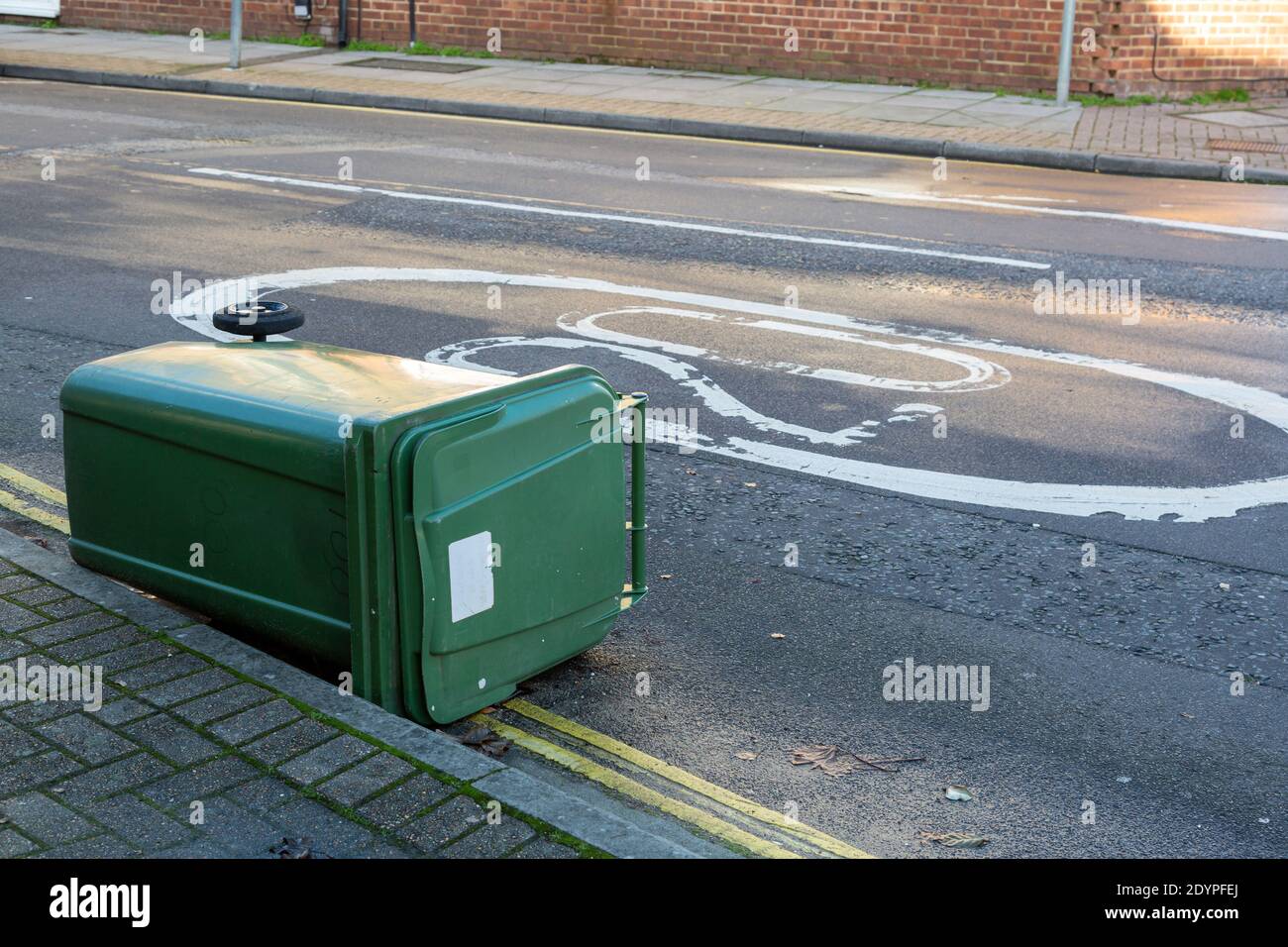 A green recycling wheelie bin blow into the road on a street after high winds Stock Photo