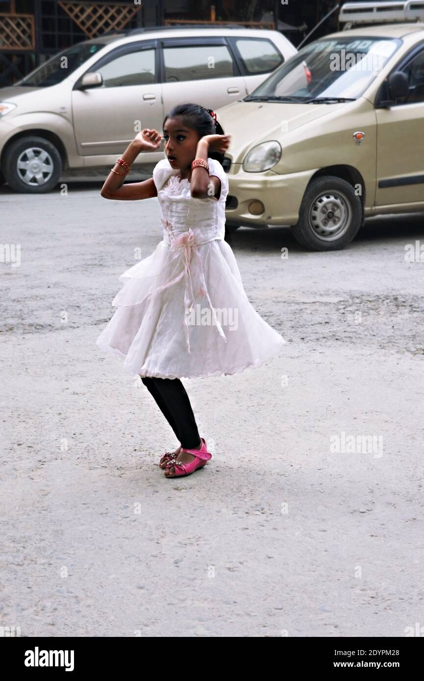 A little girl from Nepal in a white festive dress dancing on the street on the Diwali or Deepavali holiday. Pokhara Stock Photo