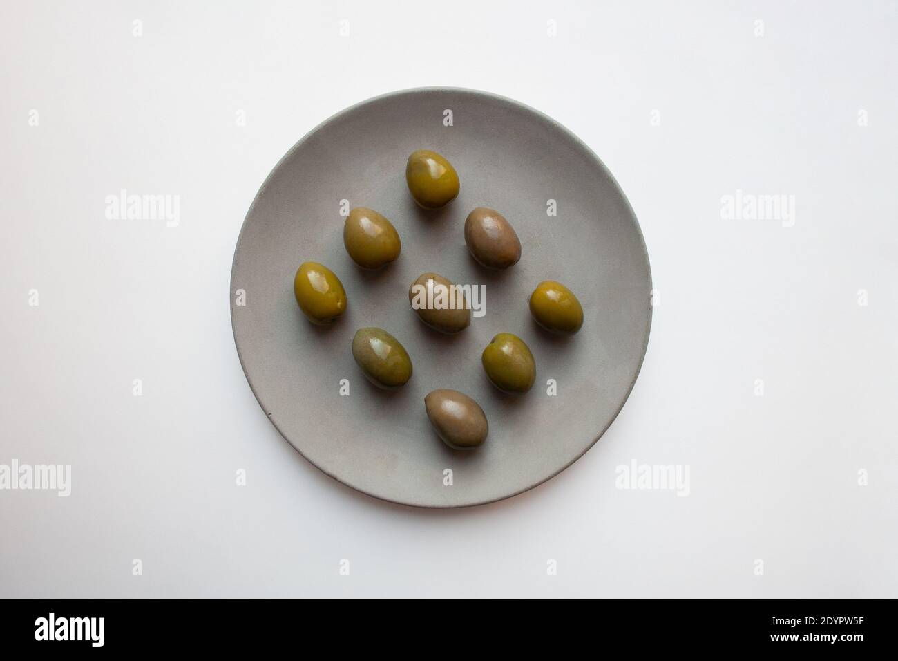 Green olives on grey concrete plate isolated on white background from a high angle view Stock Photo