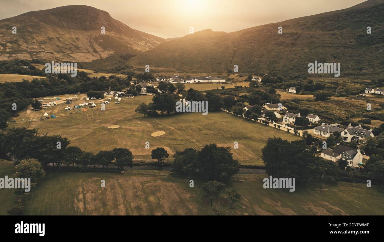 Sunset aerial at village mountain . Nobody nature landscape at sun set. Cottages, houses at road. Whiskey distillery at valley. Cinematic Loch-Ranza, Arran island, Scotland, United Kingdom, Europe Stock Photo