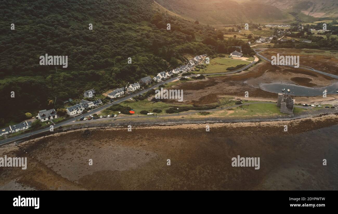 Aerial ancient castle ruins at sea shore. Nobody nature seascape at sun ocean bay. Buildings, cottages, houses at mountain. Cars at rural road. Loch-Ranza, Arran island, Scotland, Europe Stock Photo