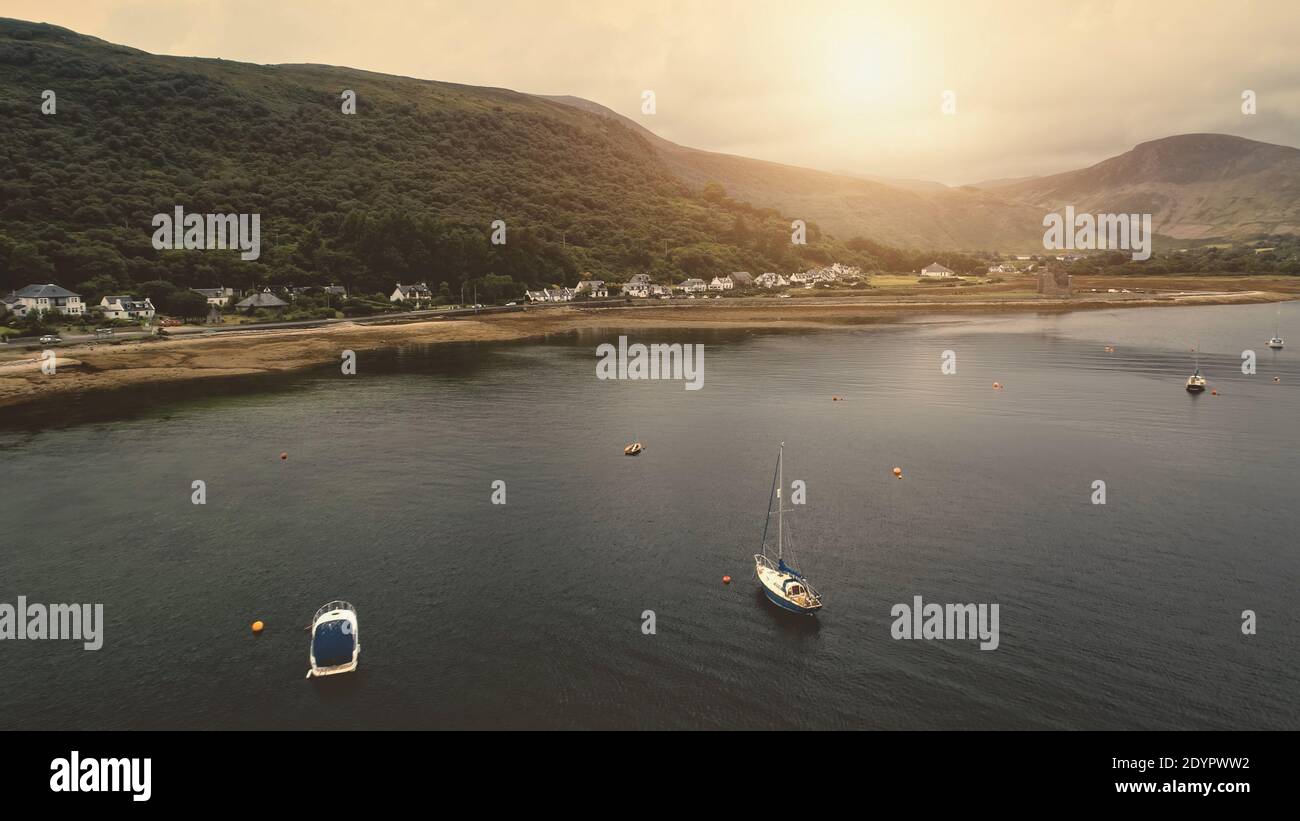 Yacht, ships at sun ocean bay aerial. Ancient castle ruins at sea shore. Nobody nature seascape. Buildings, cottages, houses at mountain. Cars at rural road. Loch-Ranza, Arran island, Scotland, Europe Stock Photo