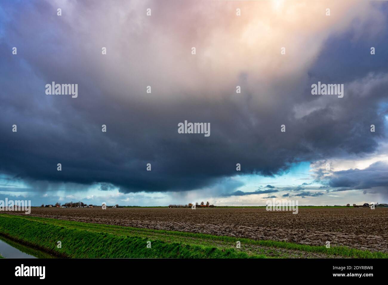 Wintry shower with fall streaks of rain and small hail over flat dutch countryside Stock Photo