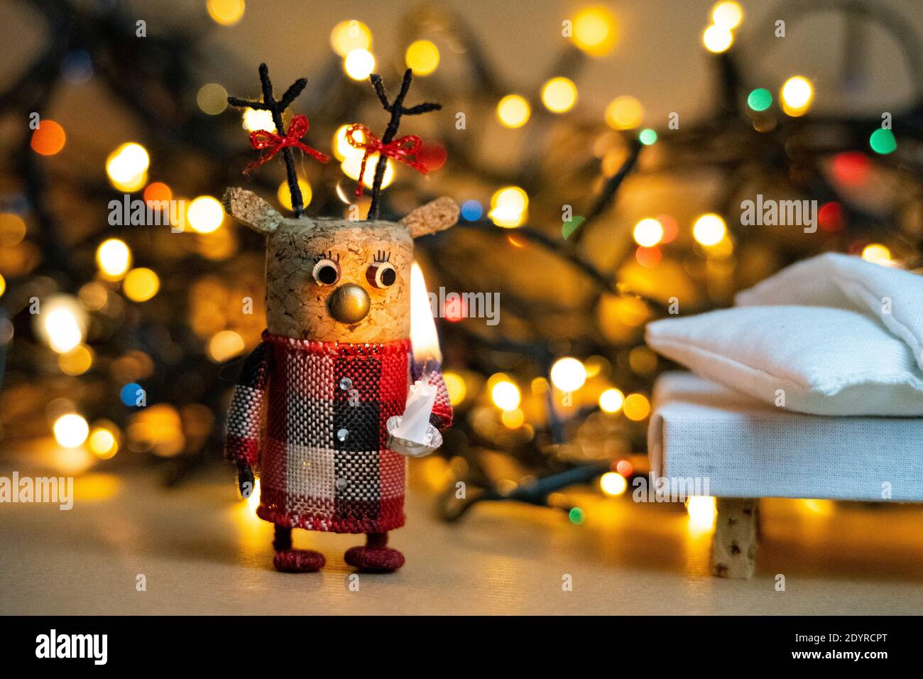 Christmas lights bokeh with a handmade deer decoration made of champagne cork holding a candle having a curious and surprised Stock Photo