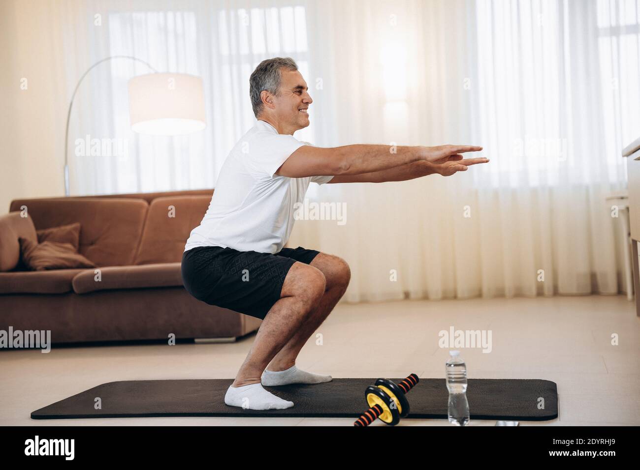 Workout time Strong senior man doing squat exercises at home in his light living room. Healthy lifestyle wellbeing and activity concept. Black and Stock Photo Alamy