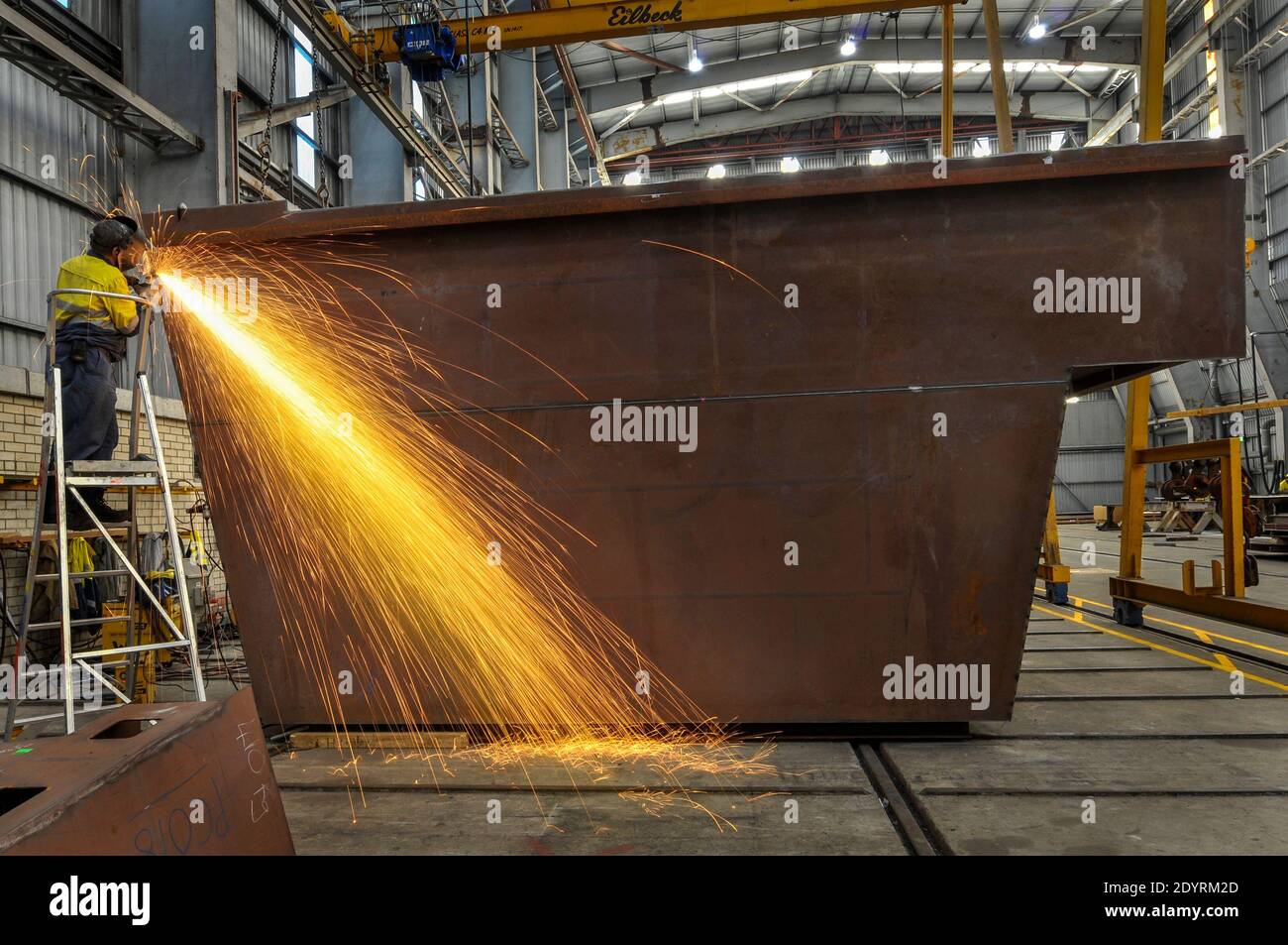 Man welding a metal structure, with a stream of sparks, in an industrial setting. Stock Photo