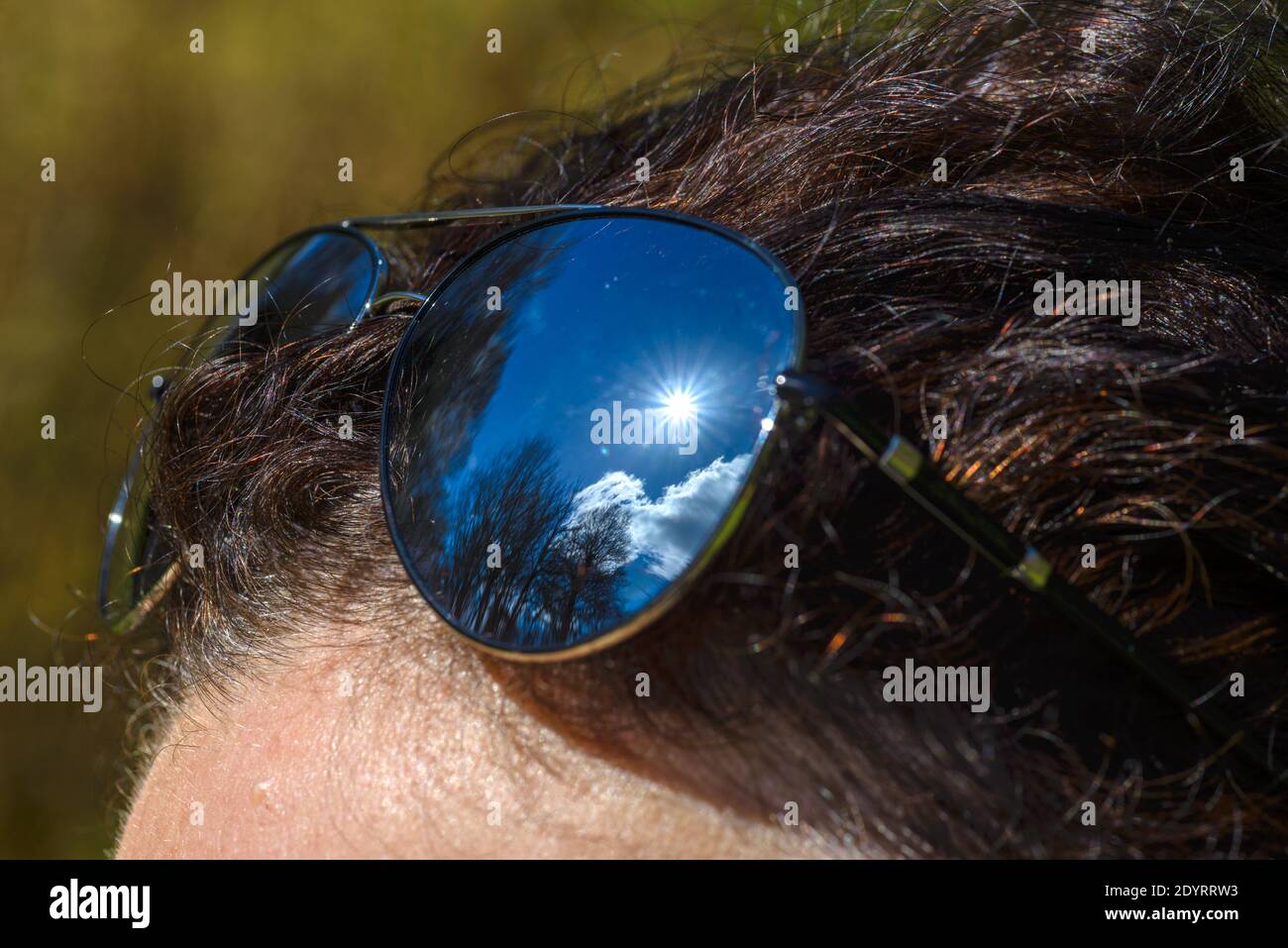 Sunglasses, with reflection of blue cloudy sky and sun, on the woman's ...