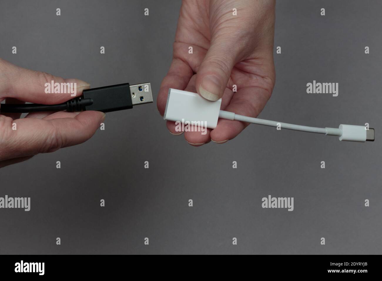hands connecting a usb cable to a usb-c to usb adaptor on a gray background Stock Photo