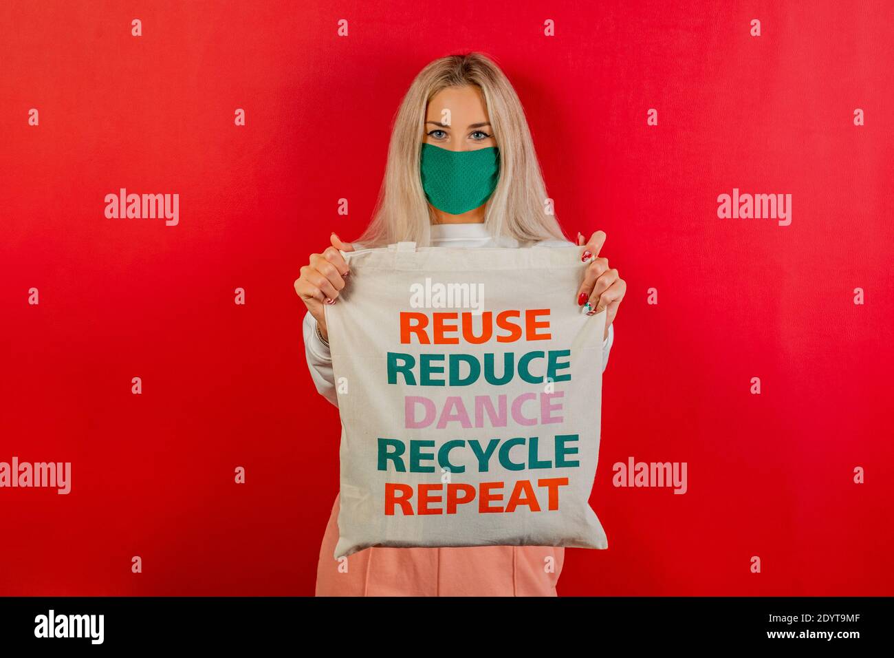 Fashionable girl shopping with recycled bag and green mask for prevention from coronavirus Covid19 pandemic. Red background. Concept recycle Stock Photo
