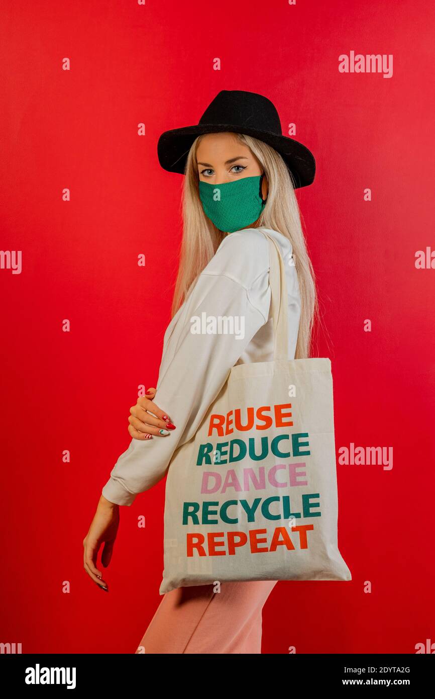 Fashionable girl shopping with recycled bag and green mask for prevention from coronavirus Covid19 pandemic. Red background. Concept recycle Stock Photo