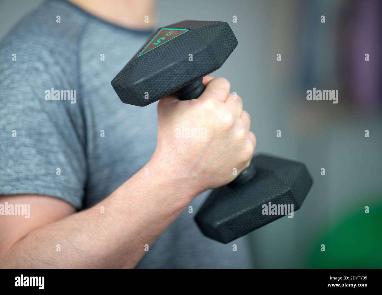 Training with dumbbells at home. A man is exercising with dumbbells at home. Hand bent at the elbow, holding the dumbbell Stock Photo