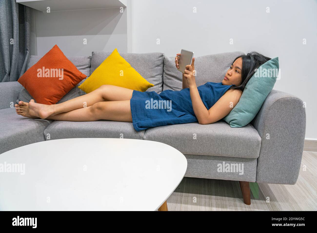 Young Asian woman lying on the sofa and using tablet at home Stock ...