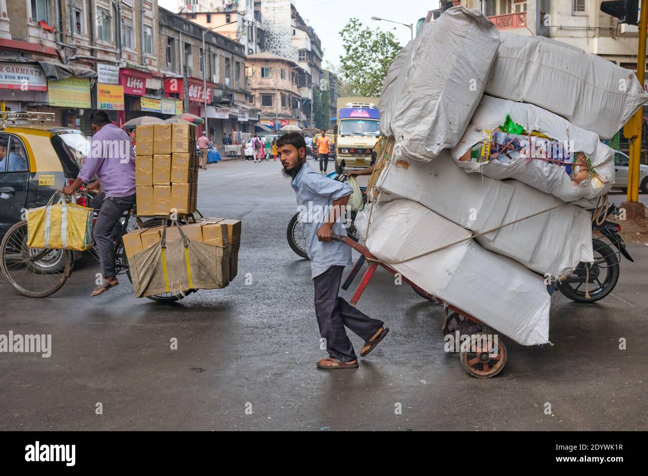 A porter pulls his handcart loaden high with textiles through Mohammed Ali Road, a main thoroughfare in South Mumbai, India Stock Photo