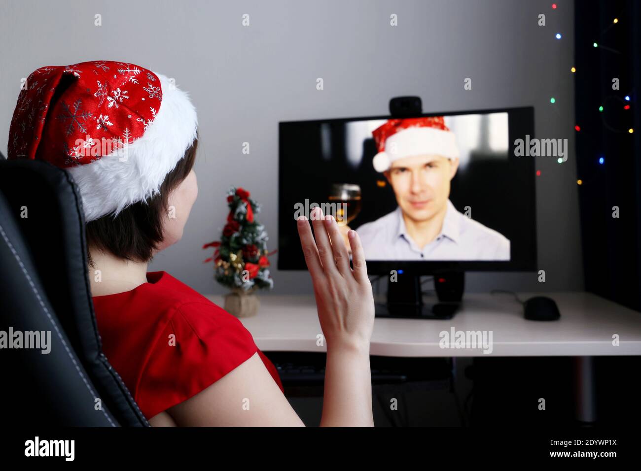 New Year celebration at a distance during coronavirus pandemic. Woman in Santa hat sitting in chair in front of PC webcam, love couple Stock Photo