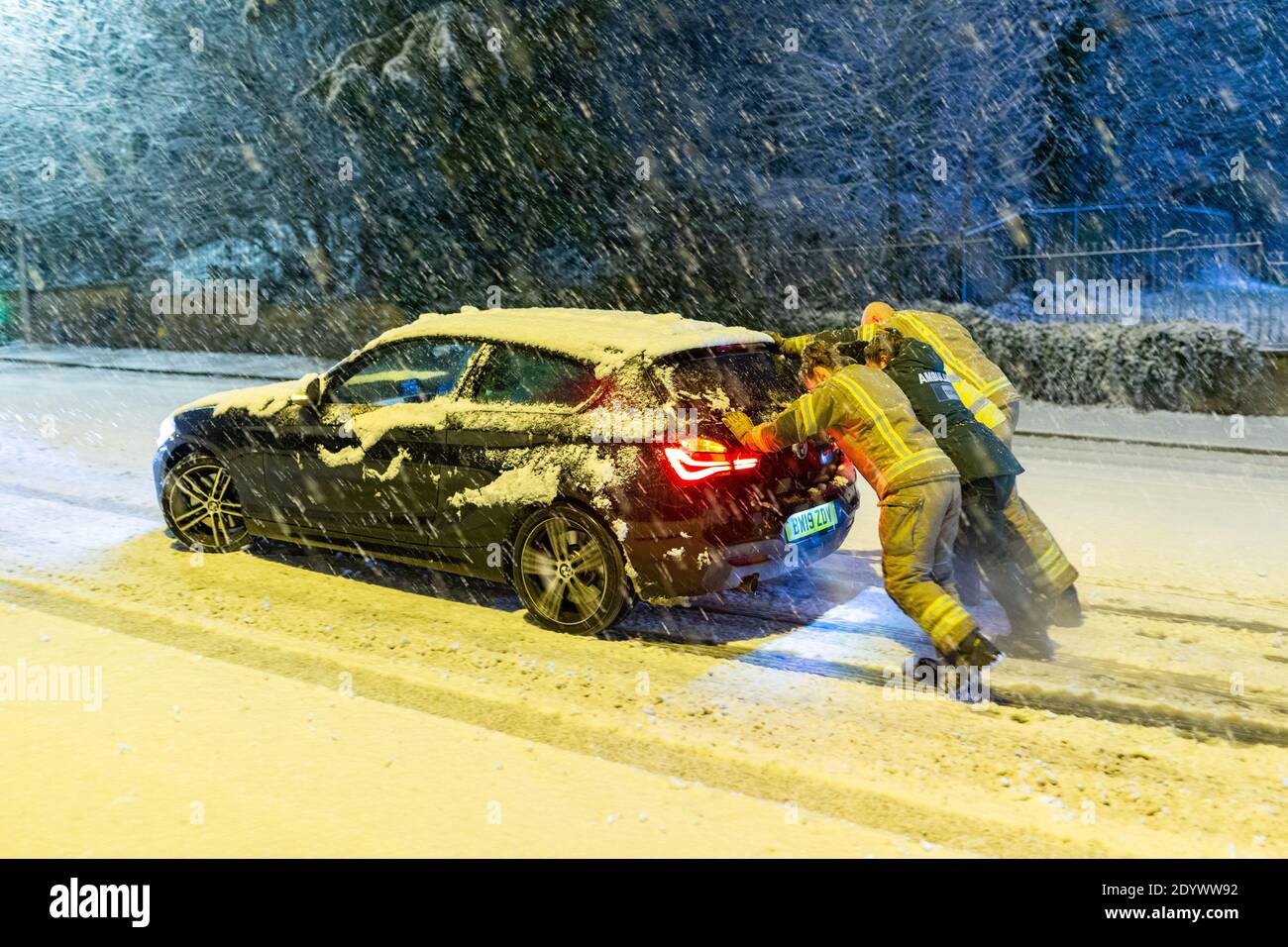 Cradley Heath, West Midlands, UK. 28th Dec, 2020. A fire crew pushes a stranded paramedic's car up a snowy hill this morning, as she tries to make it into work for her day's shift. Snow settles and causes traffic delays in Cradley Heath in the West Midlands Credit: Peter Lopeman/Alamy Live News Stock Photo