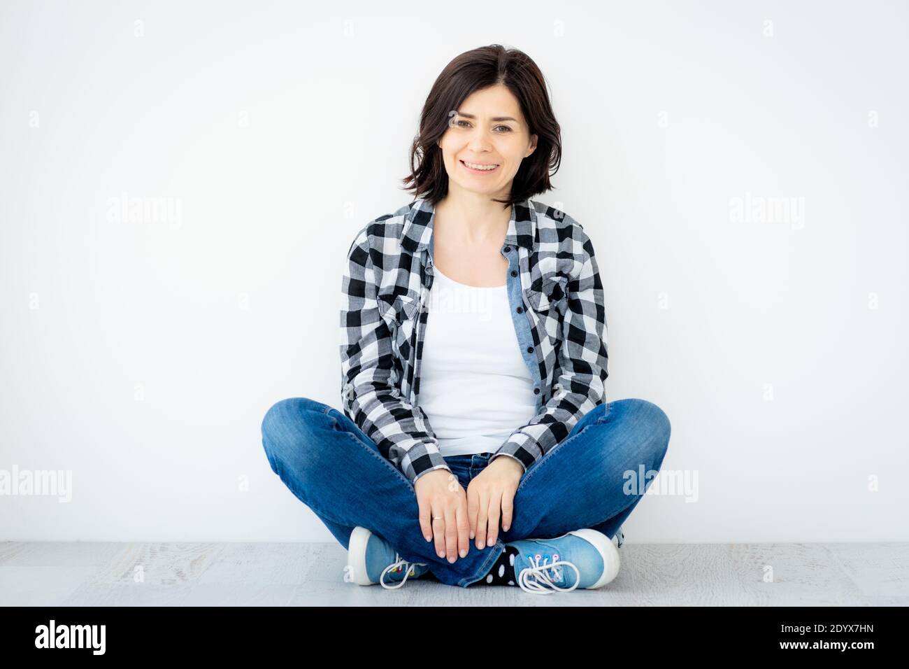 Smiling woman sitting on floor on white wall background Stock Photo