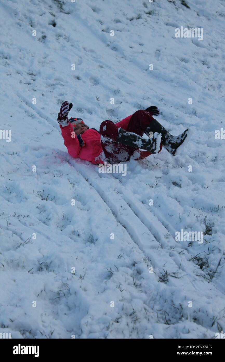Young girl sledging down a snowy bank with knees bent and arm in the