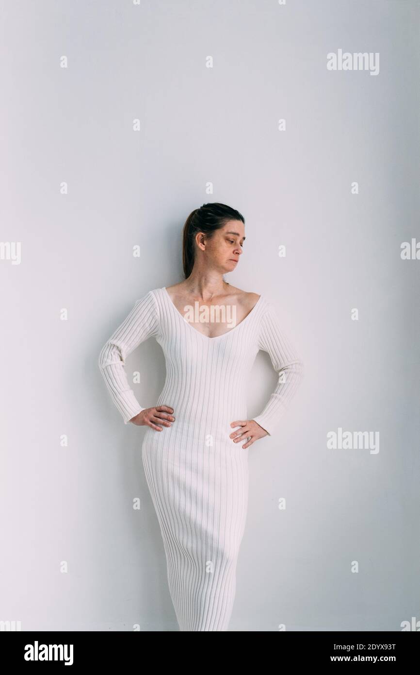 Woman wearing a long rib-knit slim jumper dress standing next to a white wall Stock Photo