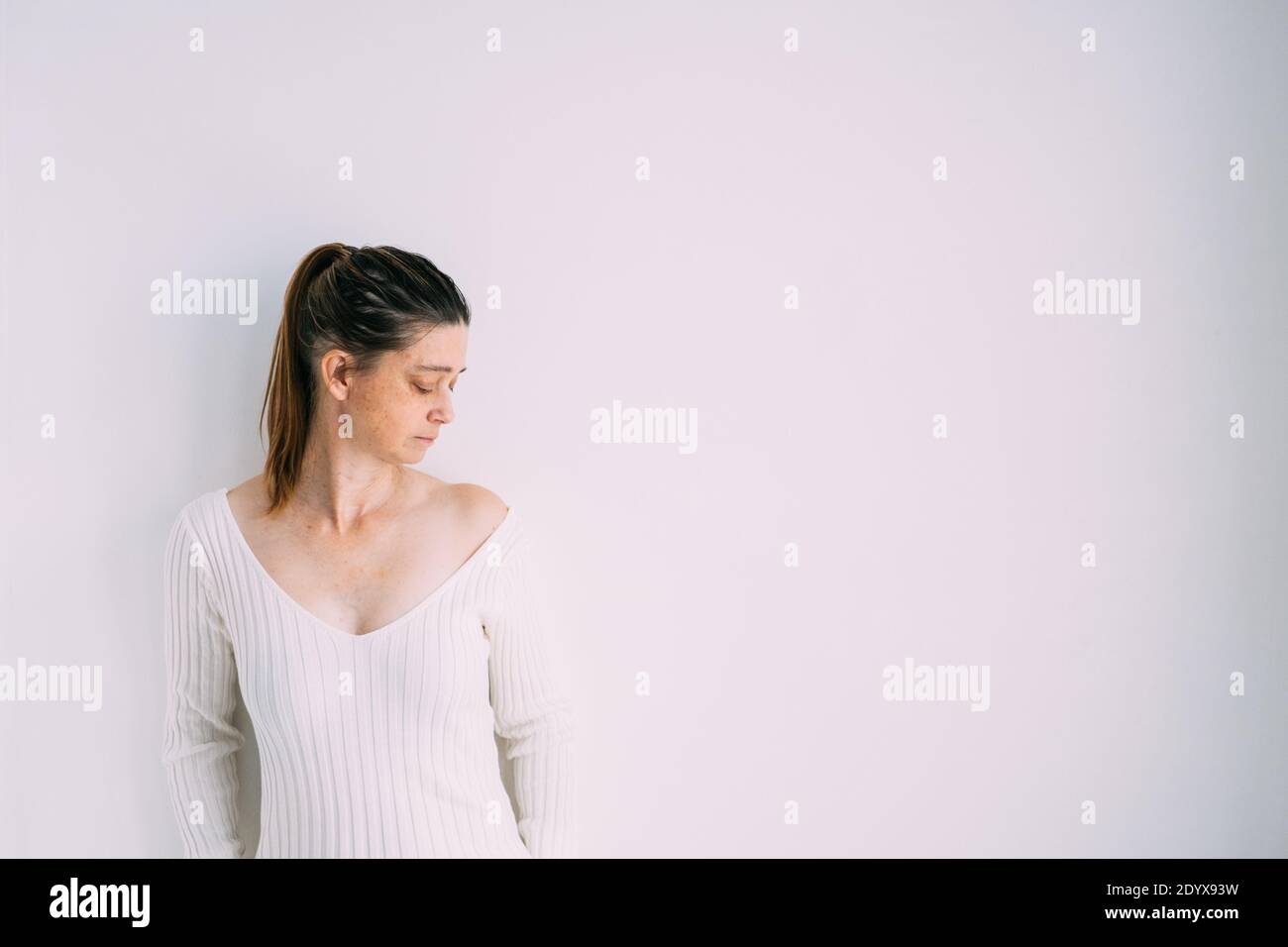 Woman wearing a long rib-knit slim jumper dress standing next to a white wall Stock Photo
