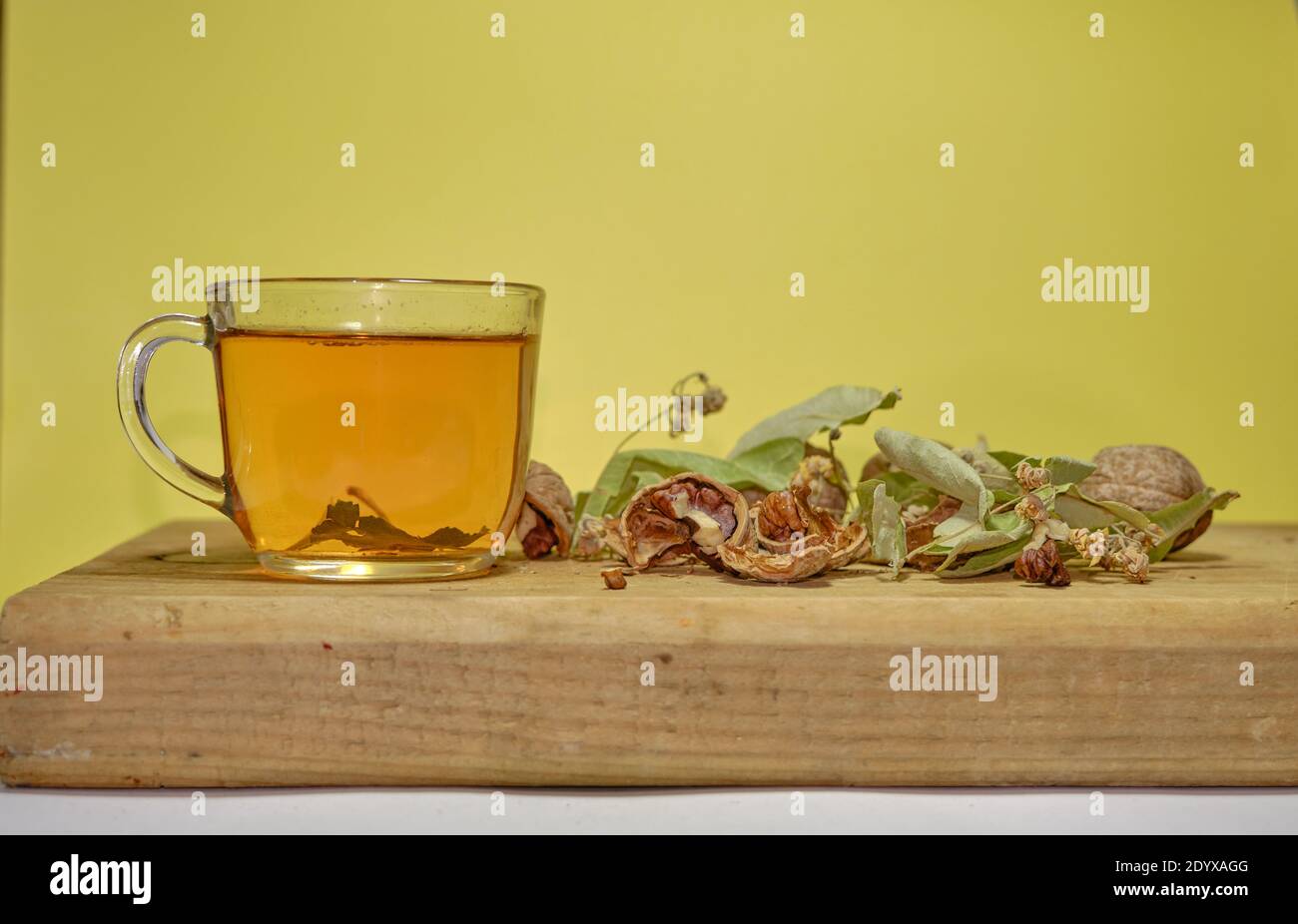 Photo of herbal and linden tea inside the glass pot together with linden tea leaves and broken and not broken walnuts on the wood table. Stock Photo