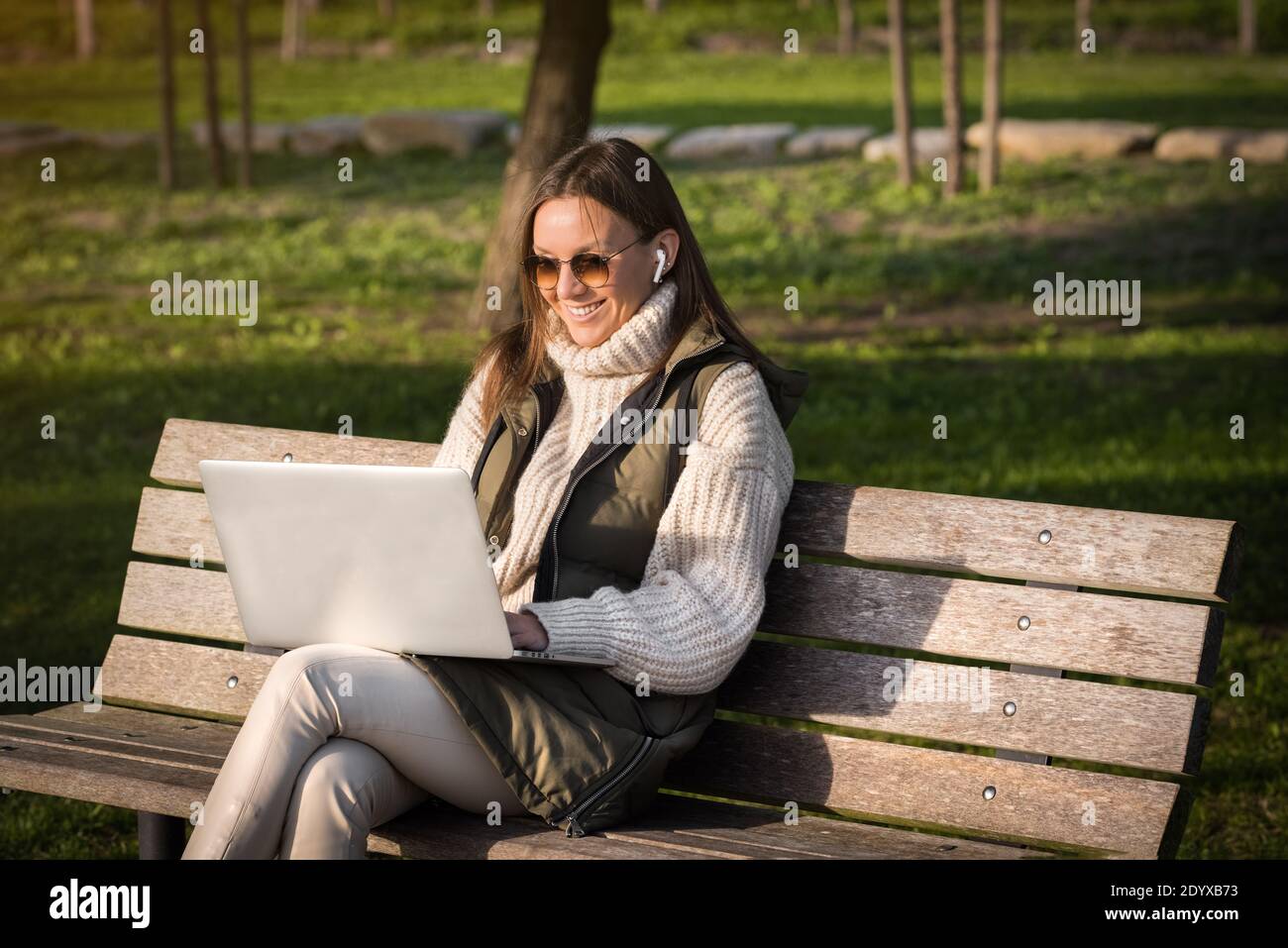 Happy woman working with laptop and headphones outdoor in city park. Student studying outdoors. Freelance working Stock Photo