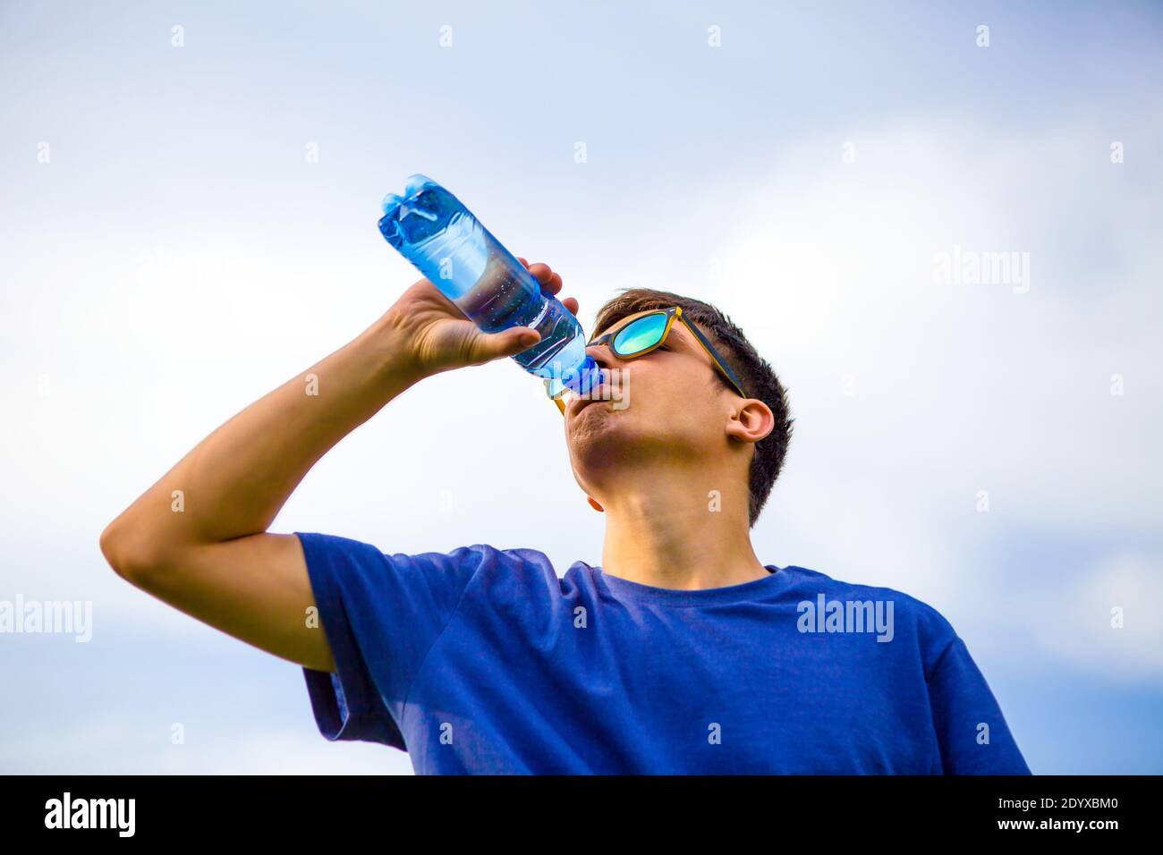 Young Man drinking a Pure Water on the Sky Background Stock Photo