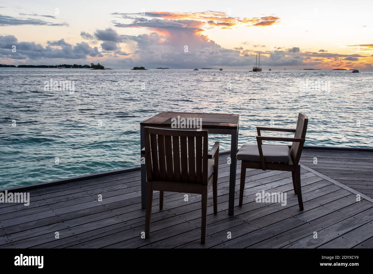 Wodden dining table on a terrace overlooking the sea, with sunset in the background, Maldives. Stock Photo