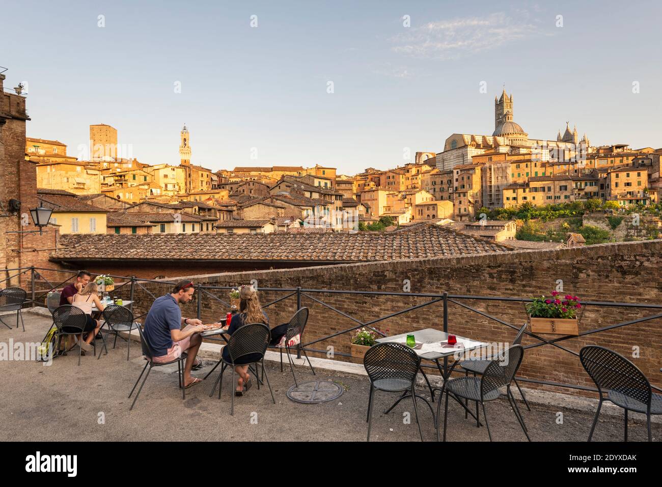 Young couples dining on the terrace of a restaurant overlooking the medieval old town of Siena in the evening sun, Tuscany, Italy Stock Photo