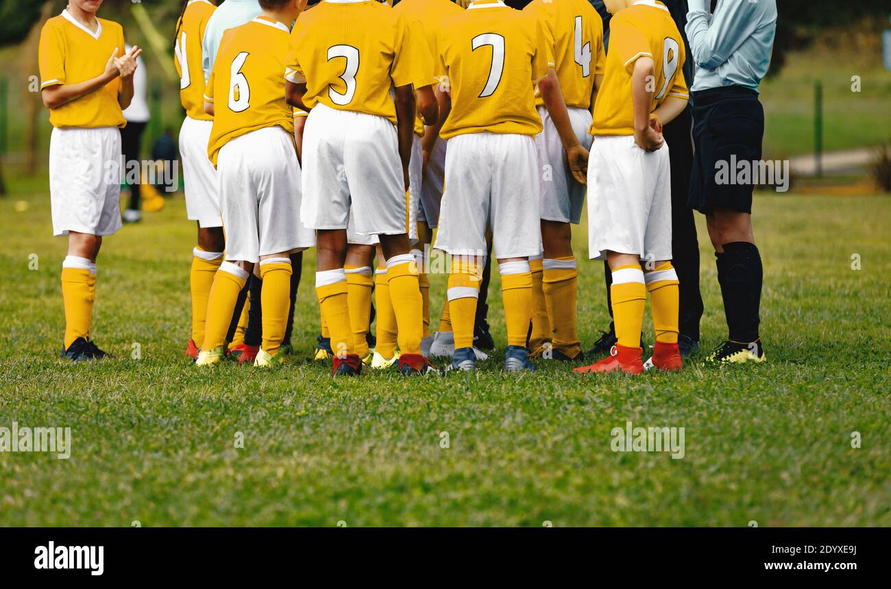 Happy boysin yellow shirts in sports team huddling with young coach