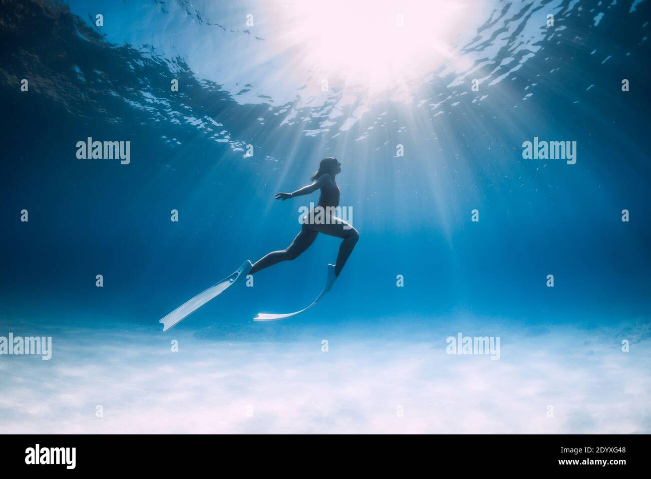 Freediver girl glides over sandy sea with white fins. Freediving with