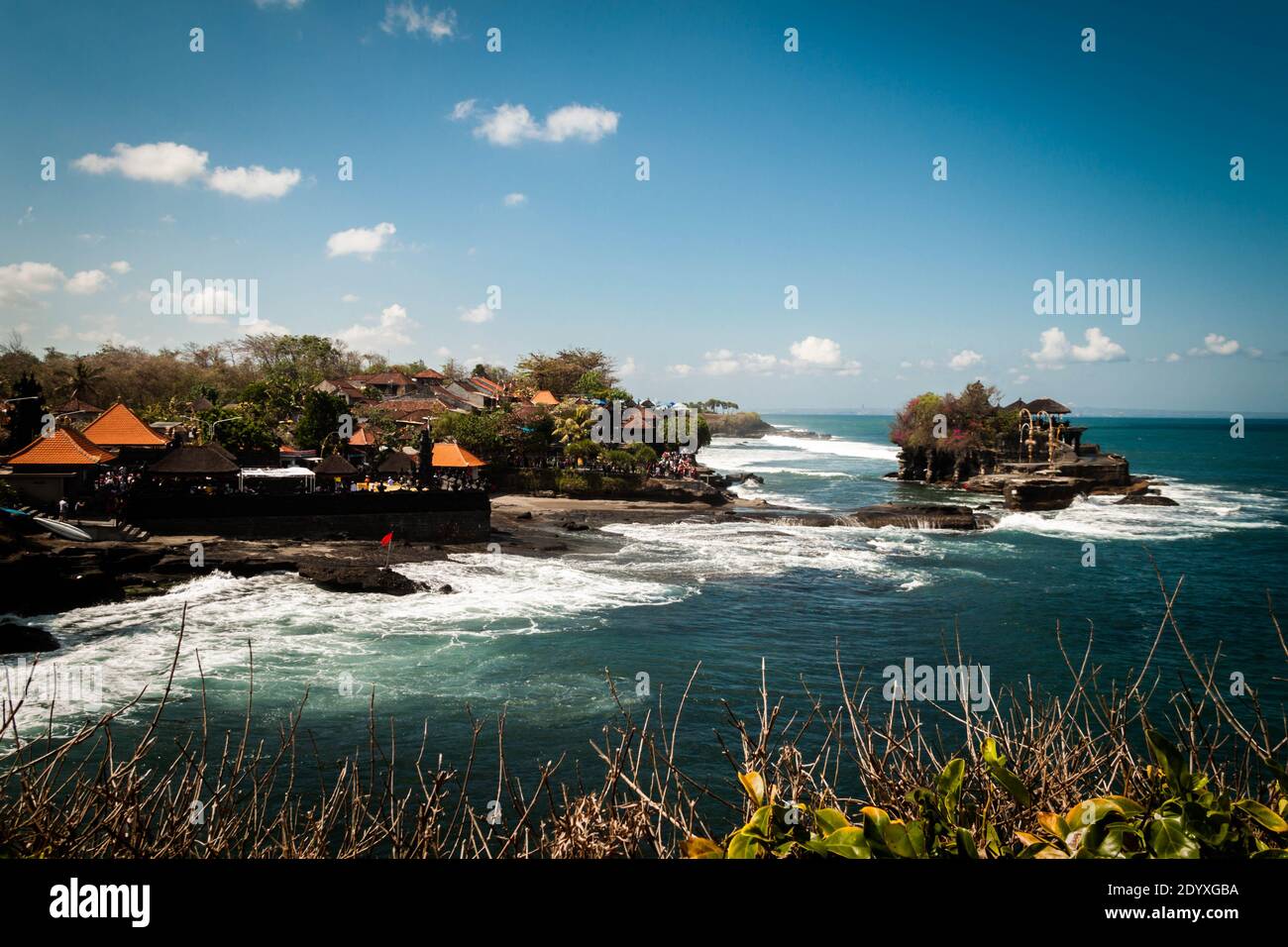Tanah Lot Temple in the wavy ocean and the restaurants on the coast Stock Photo