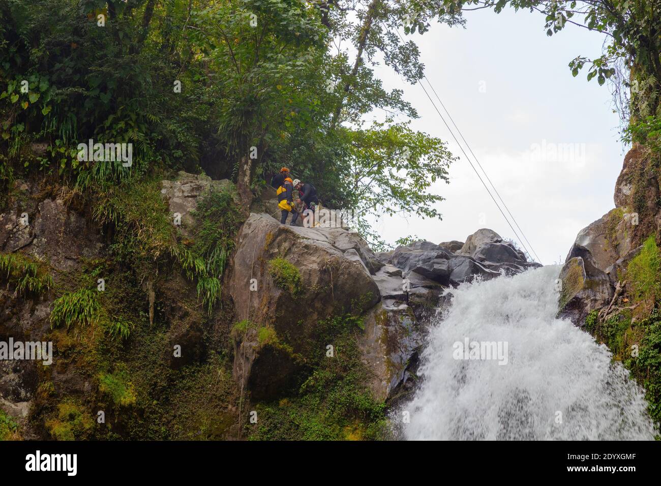 Young rock climber in a helmet and safety harness on top of a rocky ...