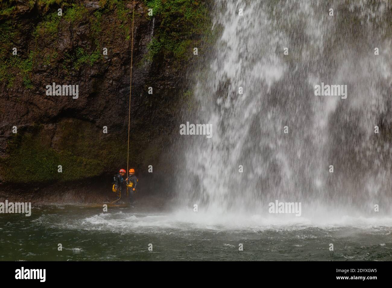 Hikers in a helmet and safety harness preparing to climb a mossy cliff ...
