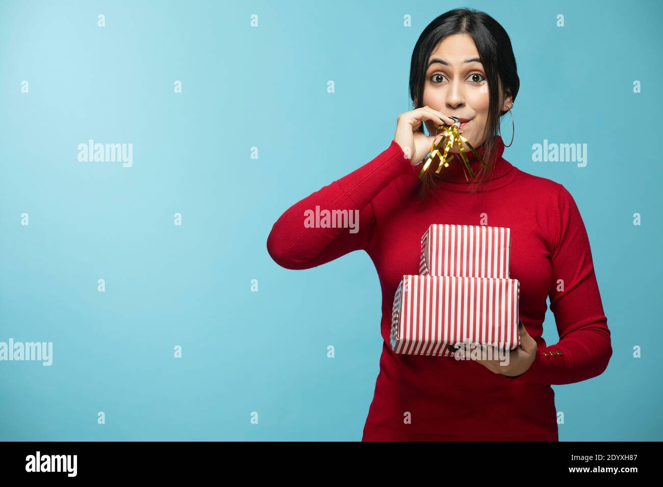 Young Female blowing party horn wearing red sweatshirt and holding gift box in hand Stock Photo