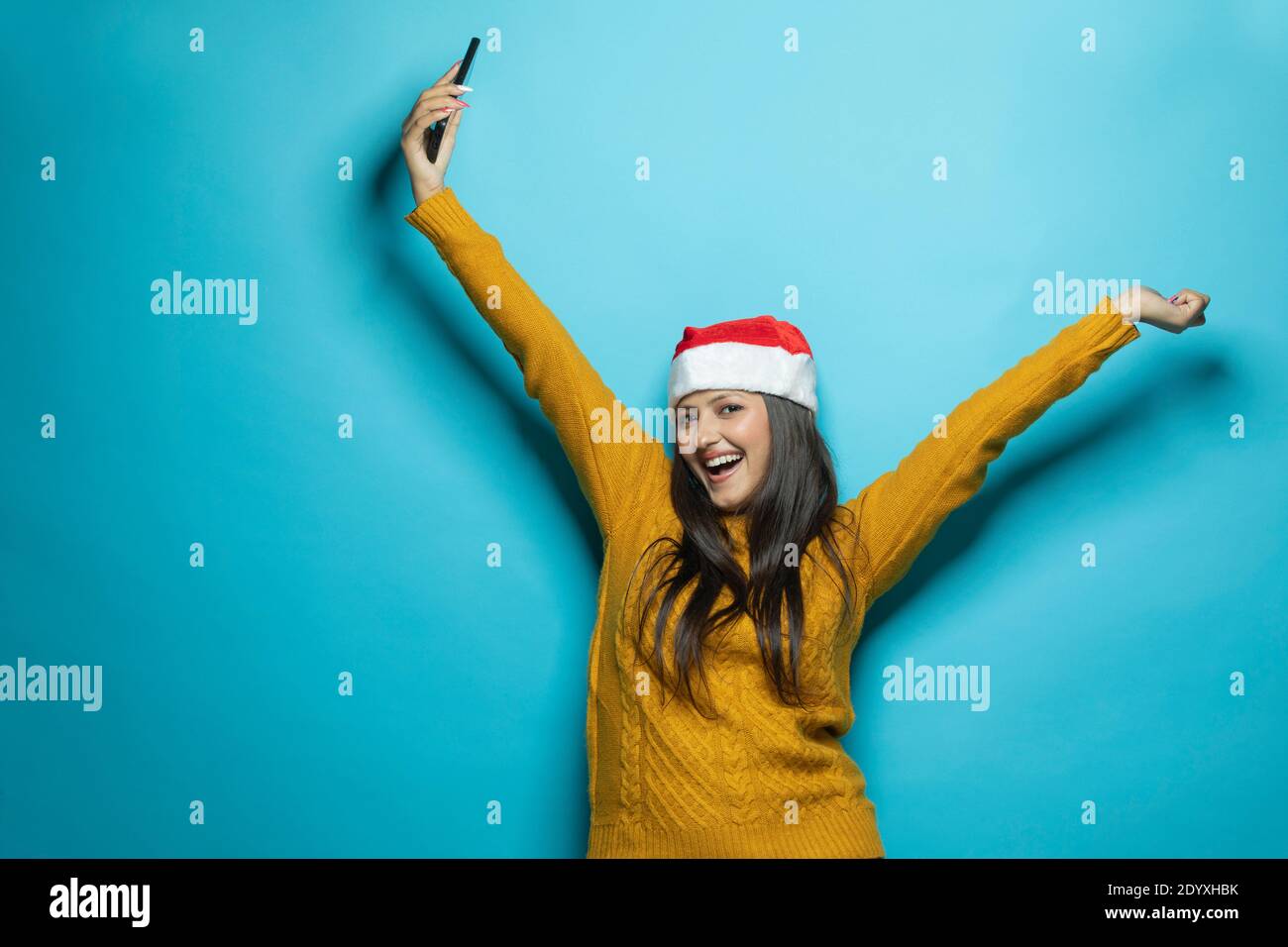 A portrait of a woman wearing Santa hat outstretched in carefree moment holding mobile Stock Photo
