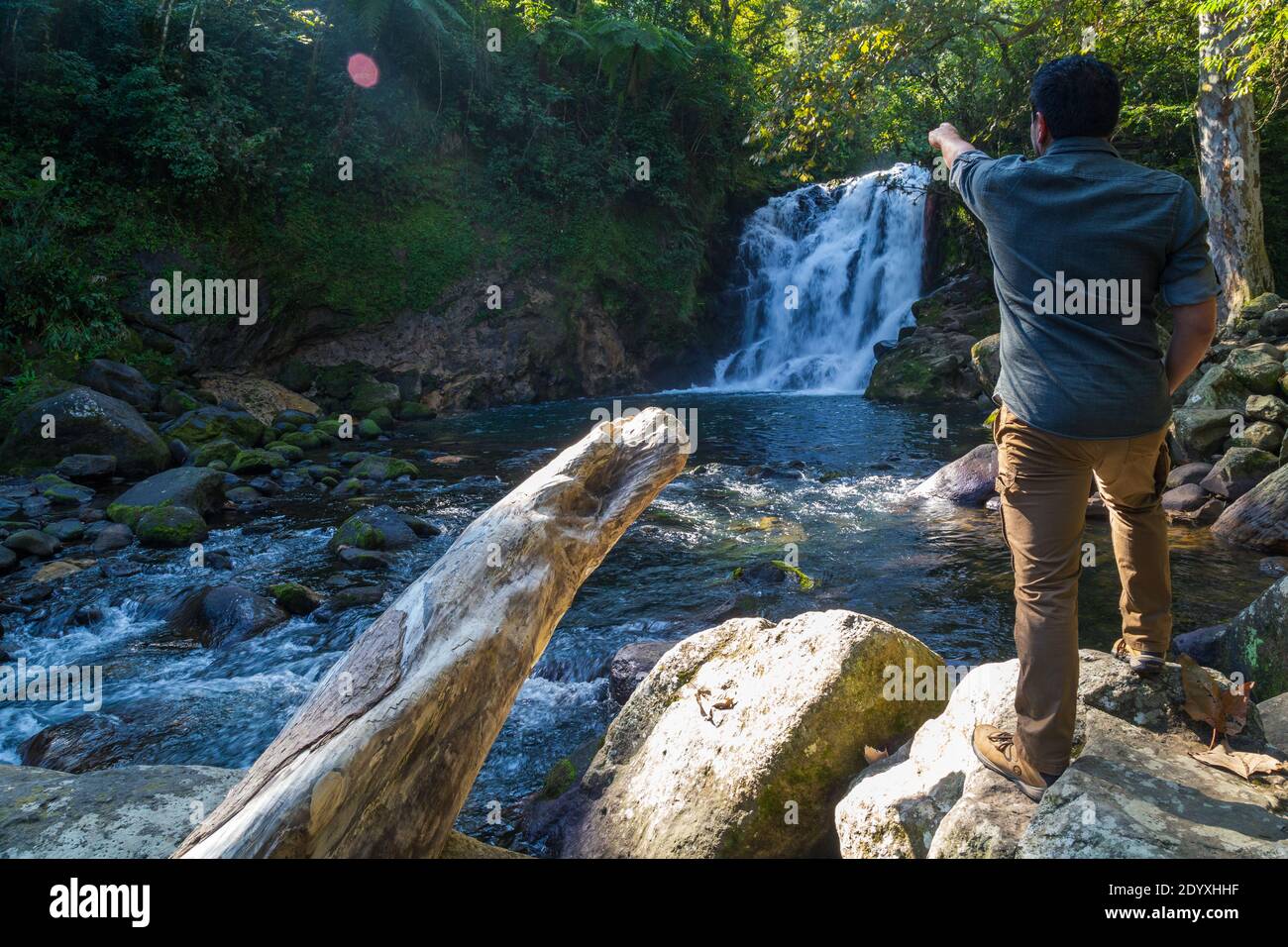 A young man standing on a rock and pointing to a waterfall in Xico, Veracruz, Mexico Stock Photo