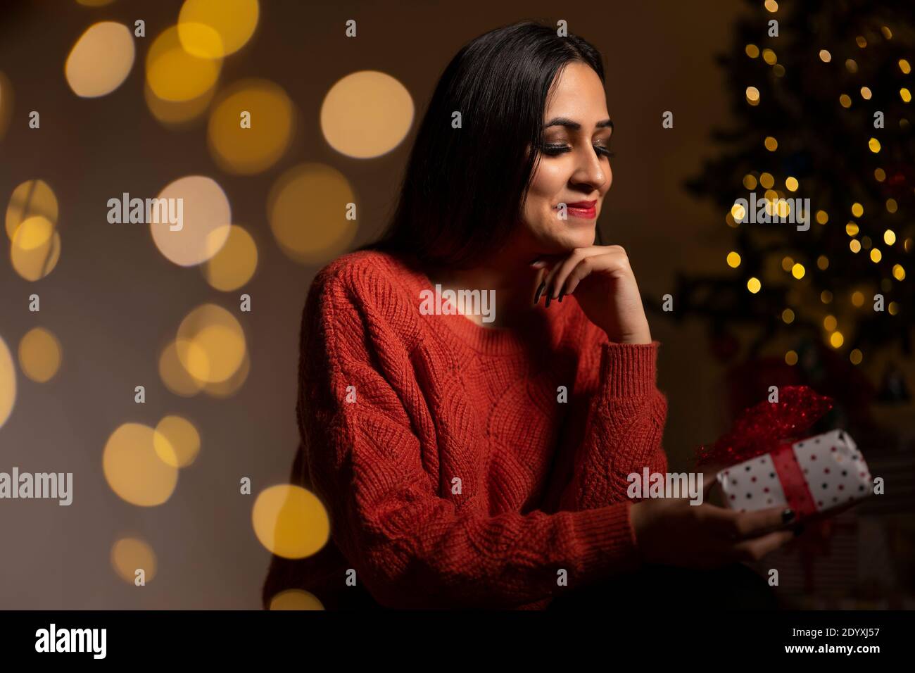 Young smiling woman in sweater holding a gift box celebrating winter holidays Stock Photo