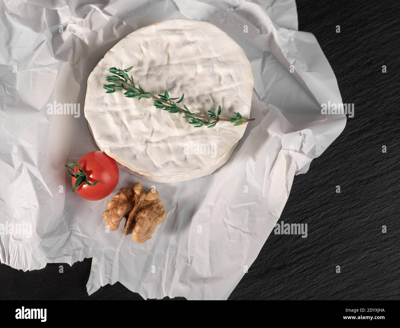 Delicious brie cheese, walnuts and tomato on paper on slate black