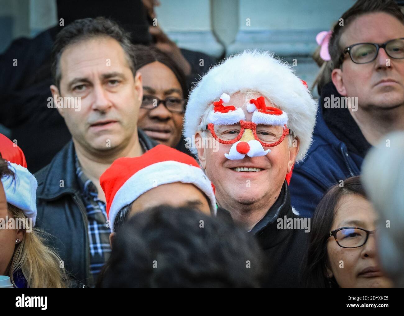 Man in Santa hat and comedy Christmas glasses, smiles in spectator crowd, London, England, UK Stock Photo