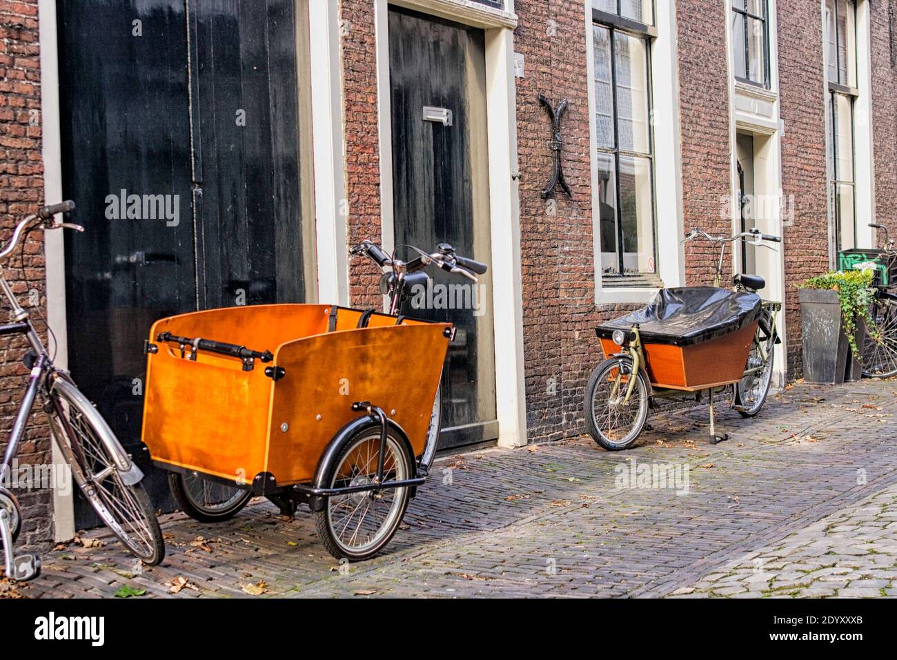 Two modern Dutch transport bikes in front of medieval homes.  Bikes are nowadays used by urban parents to bike their children to school. Stock Photo