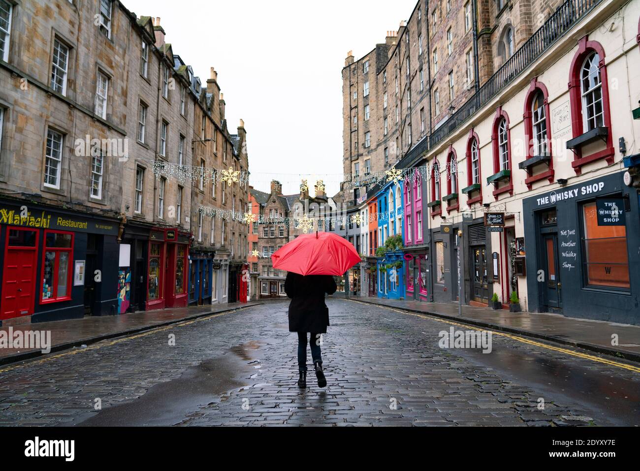 Woman holding red umbrella in rain in Victoria Street in Old Town of Edinburgh, Scotland, UK Stock Photo
