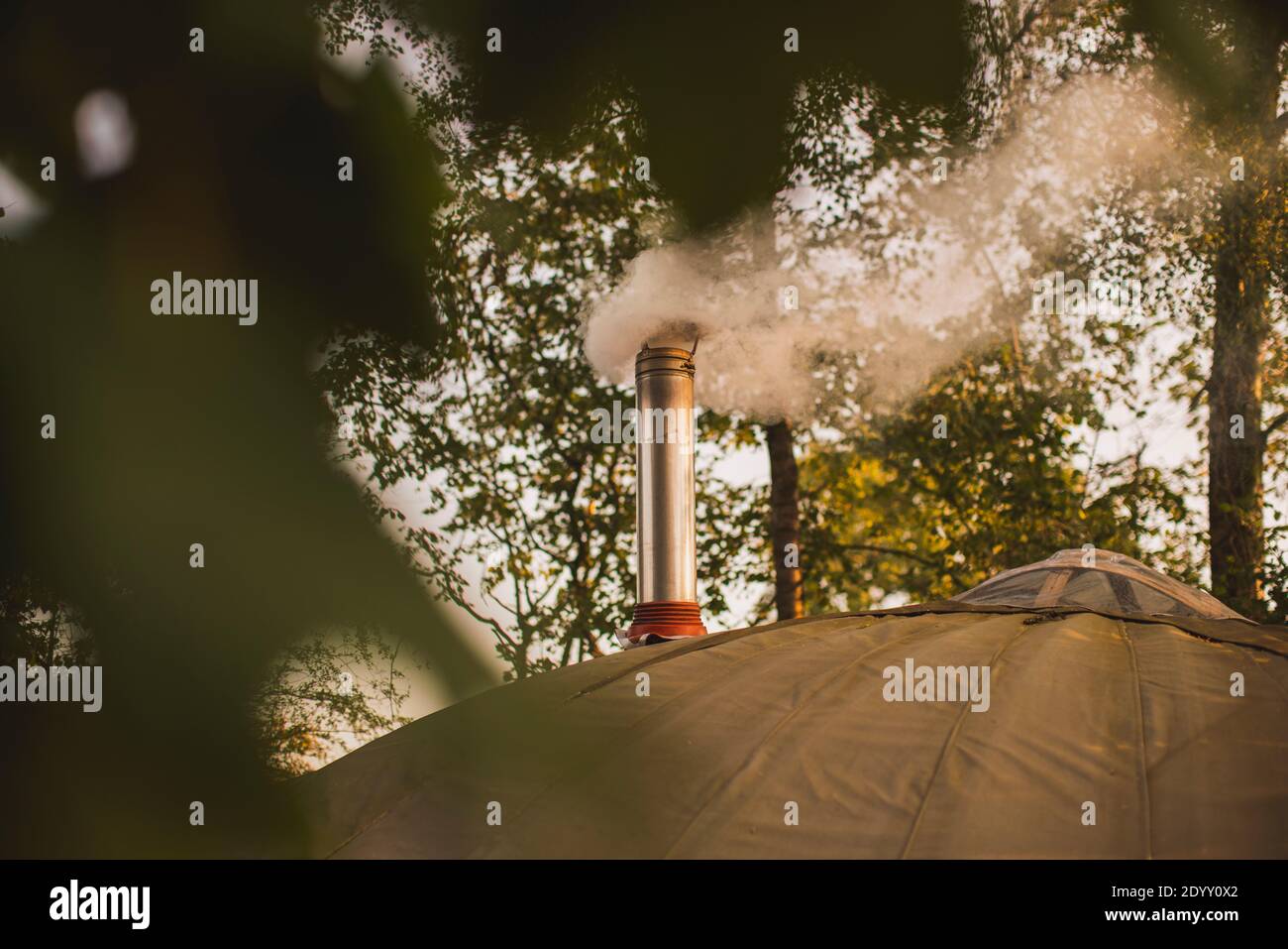 A smoking chimney from a wood burning stove installed in a yurt at a glamp site camping site. Stock Photo