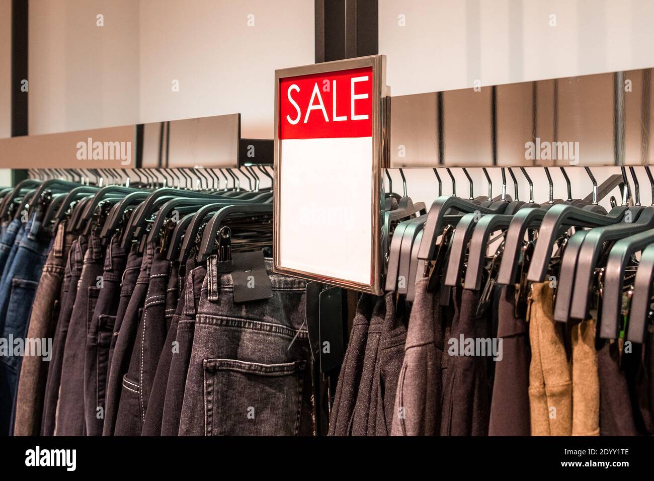 Red plate with information about the sale is above the hangers with pants in a clothing store. Promotion, advertising, shopping and black friday conce Stock Photo