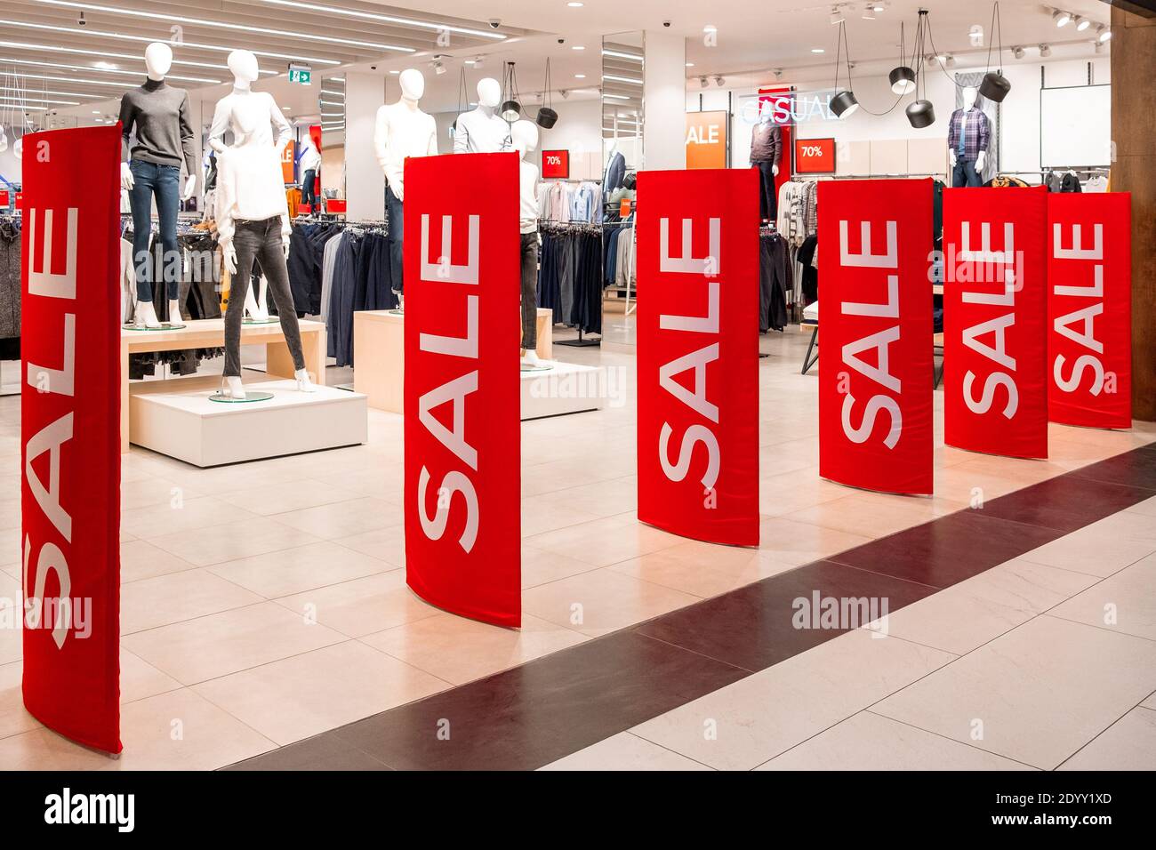 Red billboards stand at the entrance to a clothing boutique with sale information. In the background are manikins and hangers. Promotion, advertising, Stock Photo