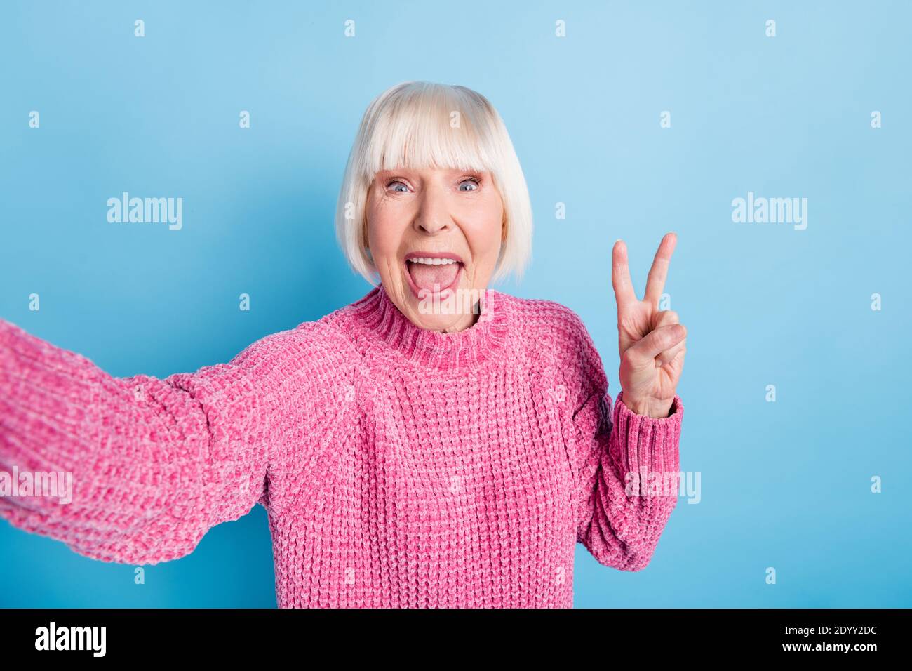 Photo portrait of excited elderly woman showing v-sign taking selfie isolated on pastel blue colored background Stock Photo