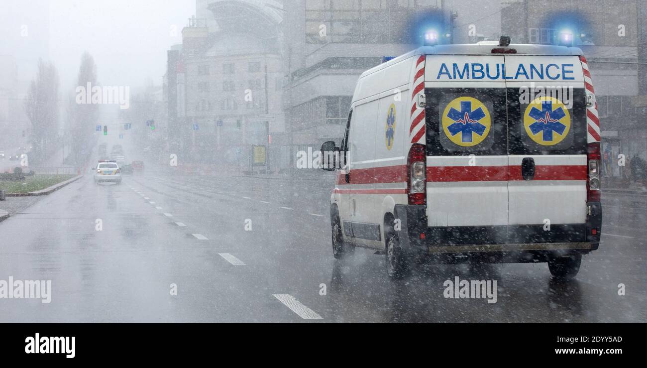Ambulance with flashing lights moves down the street in bad weather