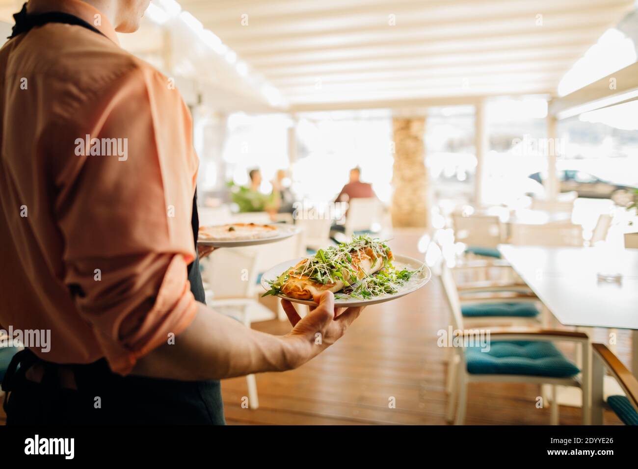 Waiter serving lunch to the distant customer.Empty restaurant due to safety restrictions. Small business working at lower capacity.No customers in the Stock Photo