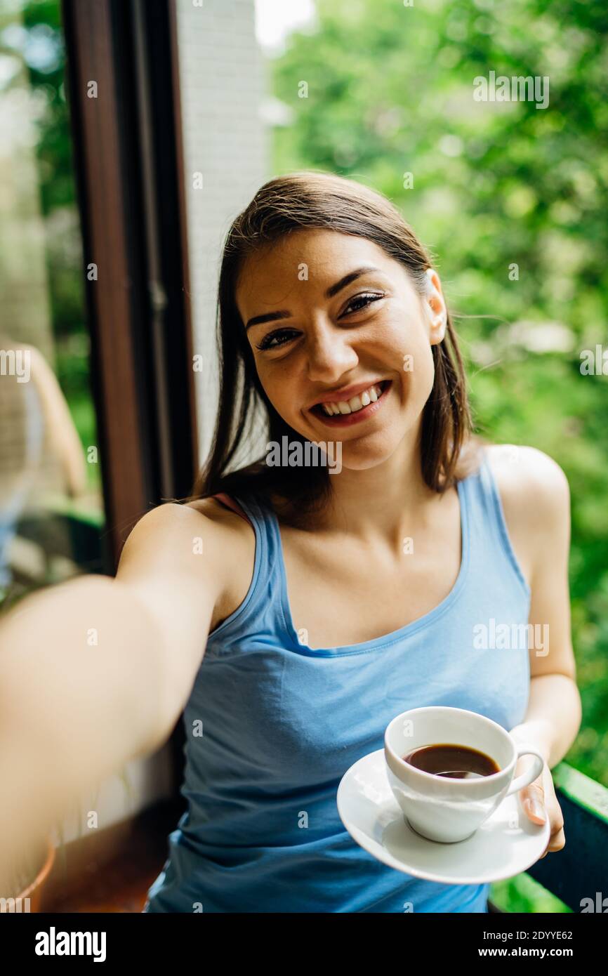 Smiling young woman taking selfie with smartphone camera.Making video call from home isolation during COVID -19 coronavirus pandemic.Online chat date. Stock Photo
