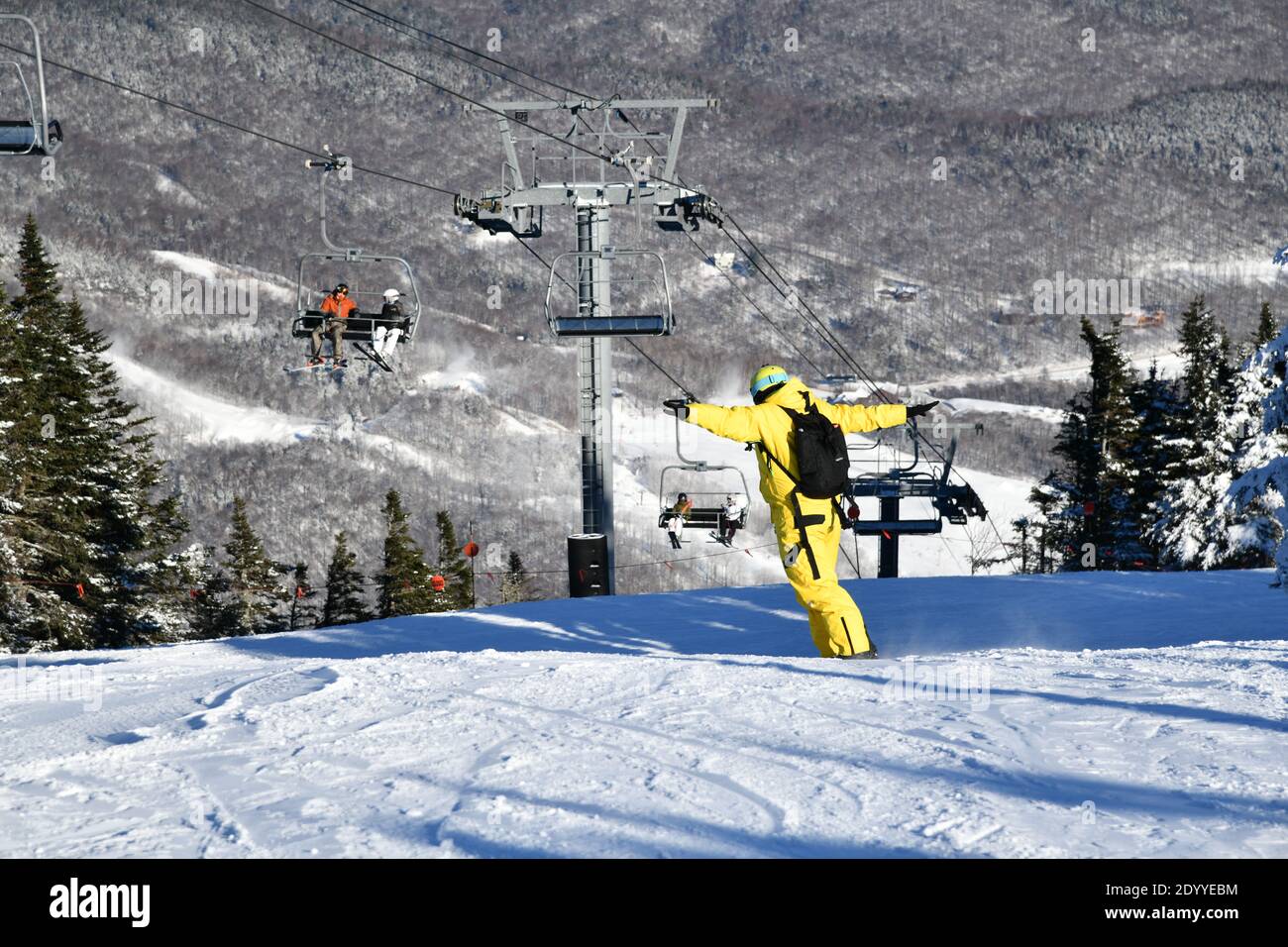 Snowboarder riding down the slopes wearing yellow mono suit on sunny day with fresh snow. Stowe mountain ski resort, VT 2020. Hi resolution image Stock Photo